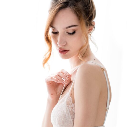 Une jeune femme tient délicatement entre deux doigts l'une des deux fines bretelles du Triangle Chantilly dentelle de calais, article de la collection lingerie de la marque Aime Couture, cératrice à Lyon